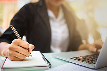 person taking notes in front of laptop